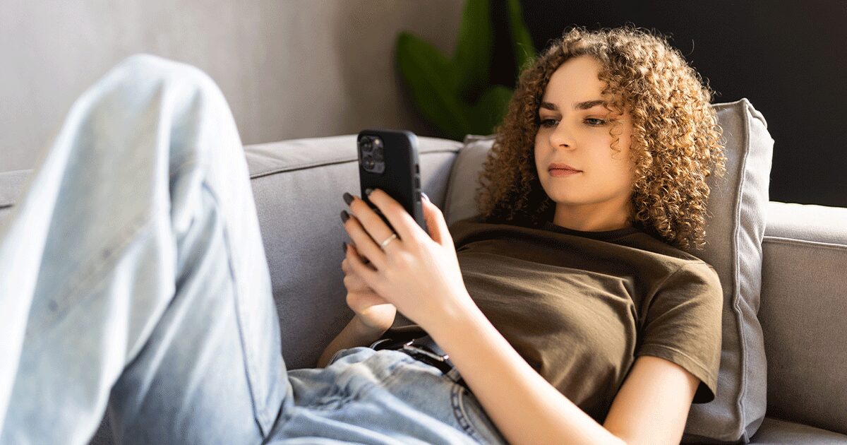 Woman sitting on a couch looking at her phone while researching the side effects of the abortion pill